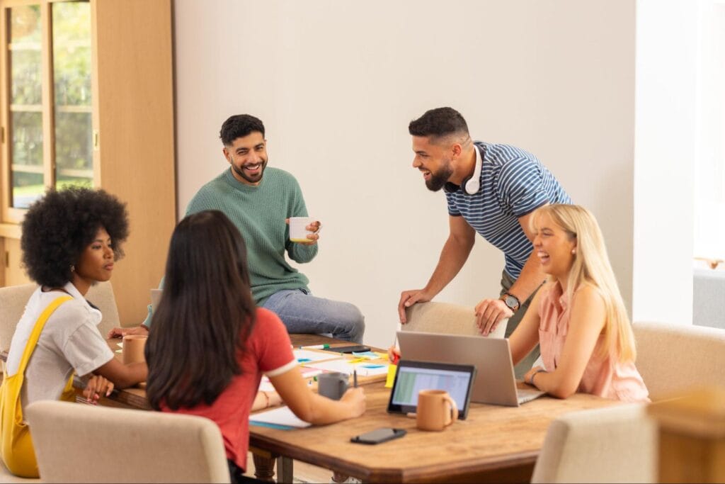 Team collaborating at a modern workspace around a table with laptops and coffee.