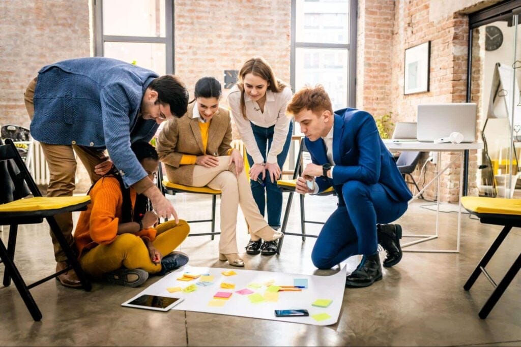 Team brainstorming session with diverse group sharing creative ideas on a floor workspace.